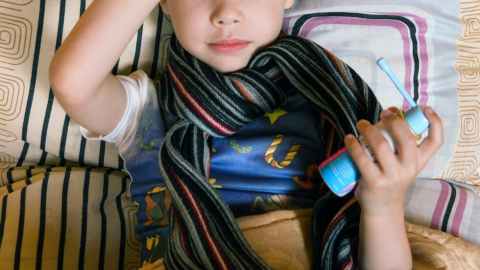 sick boy touching head and holding aerosol drug